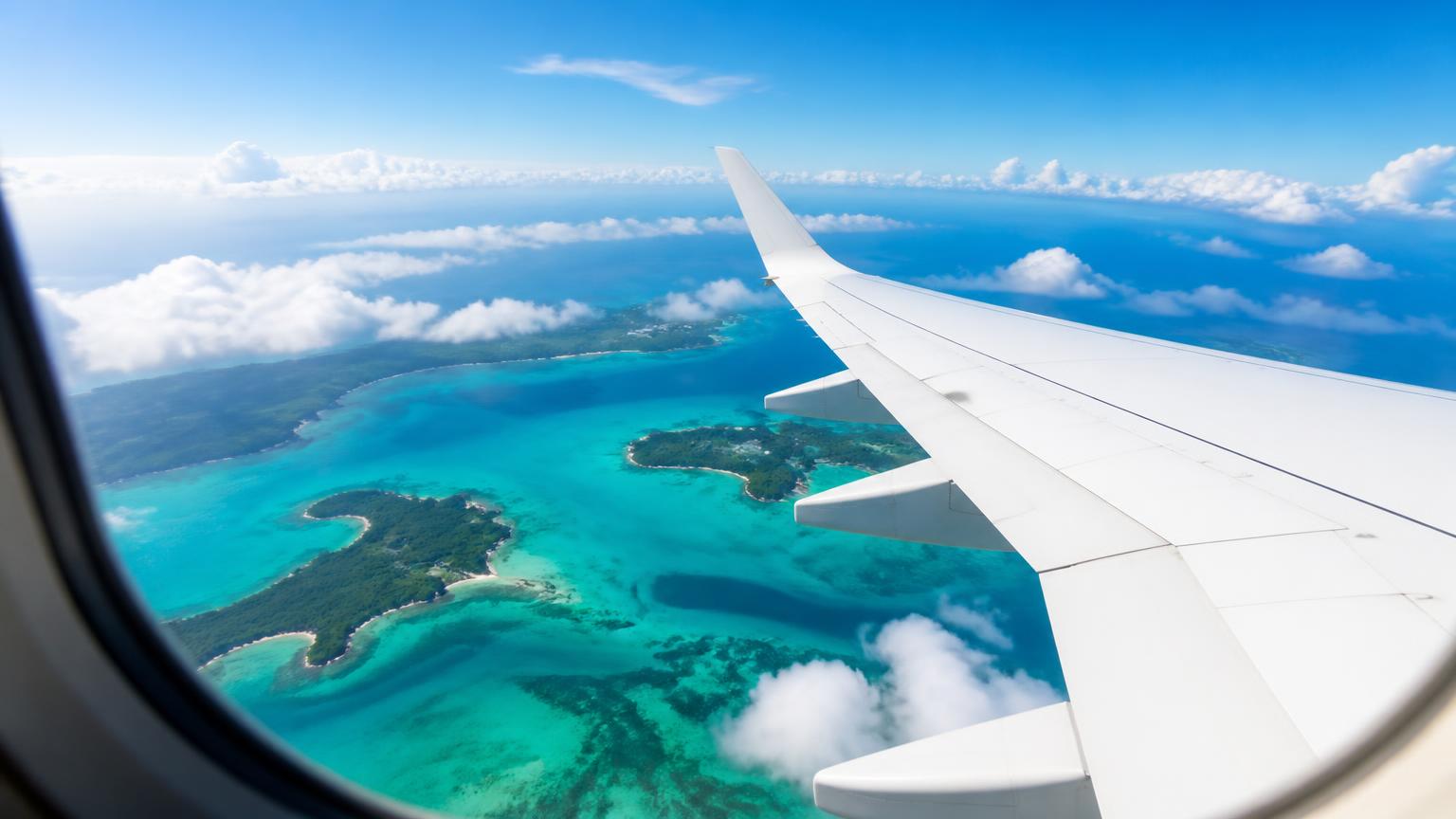 View from an aircraft window over a plain white wing, above turquoise Caribbean shallows and green islands