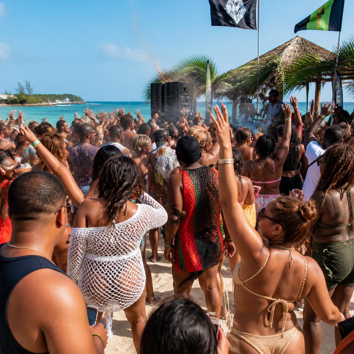 Beach party crowd dancing on white sand by turquoise water